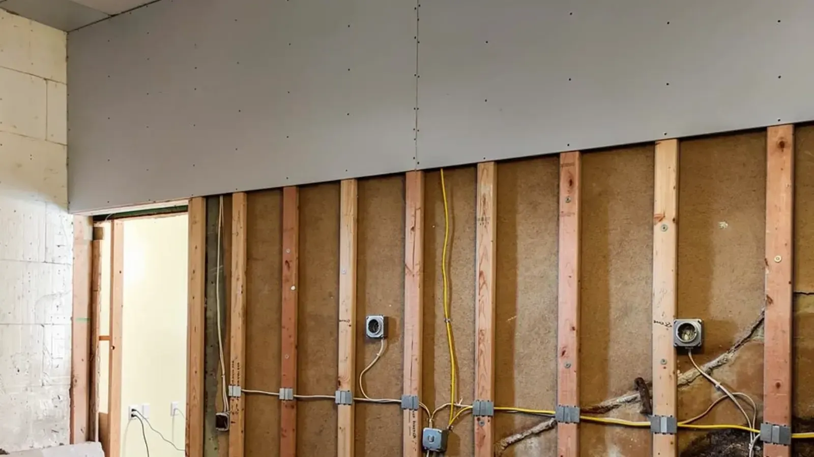 Bare gypsum drywall hung across the upper half of an interior wall, the lower stud bays still open with insulation and electrical boxes visible